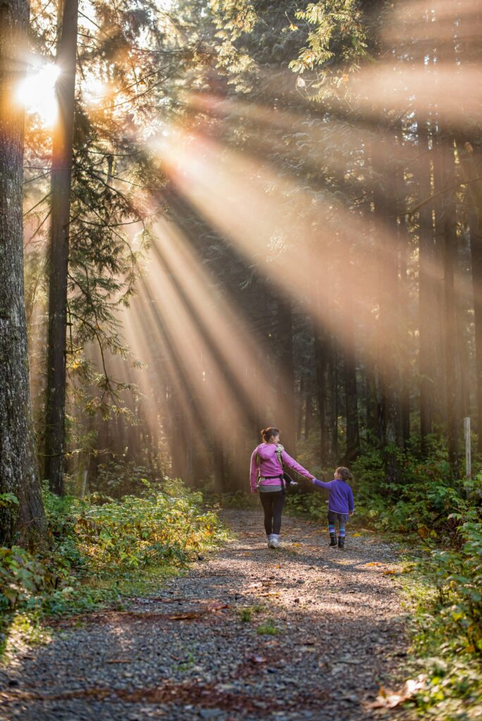 Woman hiking with a child in a bright forest in the comox valley of British Columbia